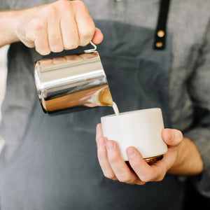 Barista naleje mlieko z leštenej kanvice z nehrdzavejúcej ocele, súčasť Espresso príslušenstva a mliečnej kanvice, všetko o káve.
