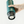Prenosný kávovar v lesnej zelenej farbe s prispôsobenou časťou na kapsuly, ideálny na ručné prípravy vonku a pre milovníkov kávy.